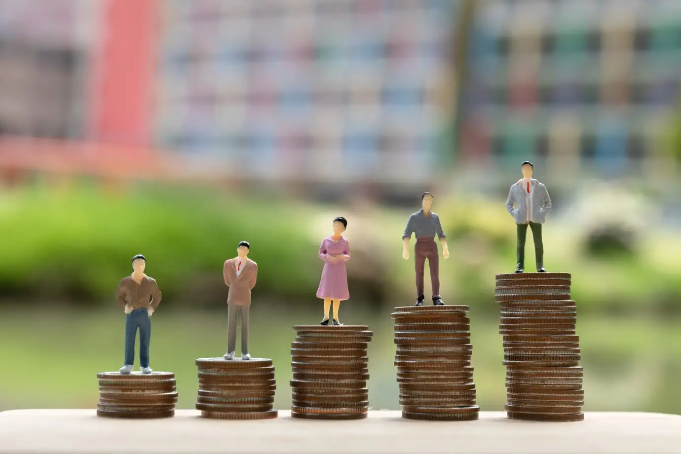 Representación visual de la brecha salarial con figuras en miniatura sobre pilas de monedas. La justicia laboral incluye la lucha por salarios equitativos.