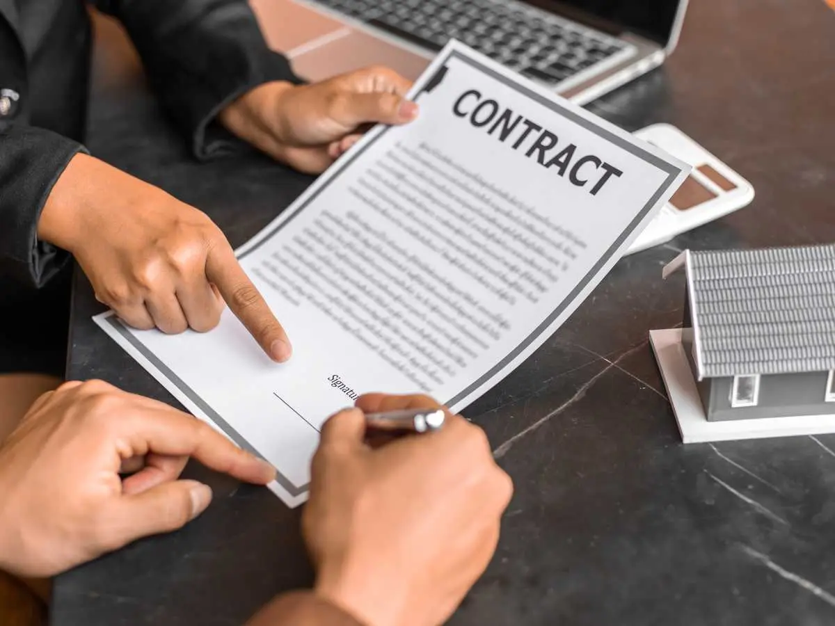 Persona firmando un contrato legal mientras otra persona señala la línea de firma, representando el concepto de IUS Variandi en acuerdos contractuales.